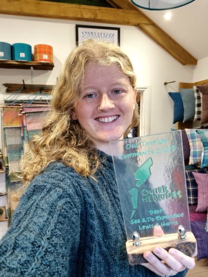 A woman with blonde curly hair smiles while holding an award.