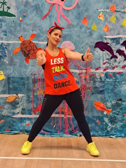 Mailen Vásquez de Palmero wearing colourful fitness gear for her Aberdeen Zumba classes, her arms are held out in front of her with her thumbs up