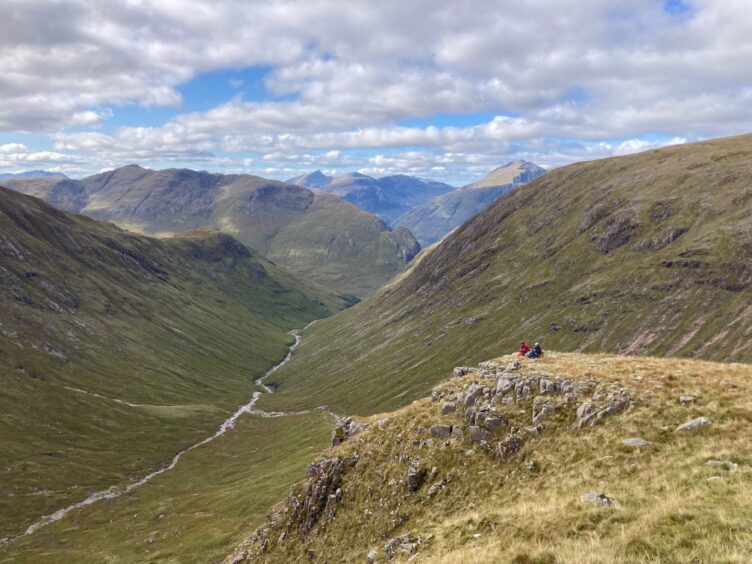 Mountaineers sit gazing out over the vast landscape of Glencoe.