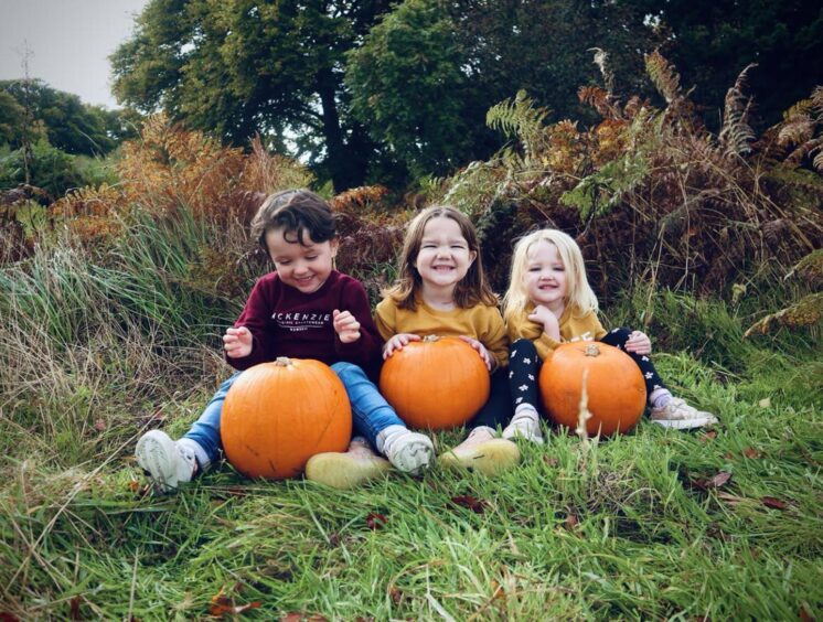 Four-year-old Josie (right) pictures with her twin brother Jude and older sister Adeline, aged seven playing with pumpkins. 