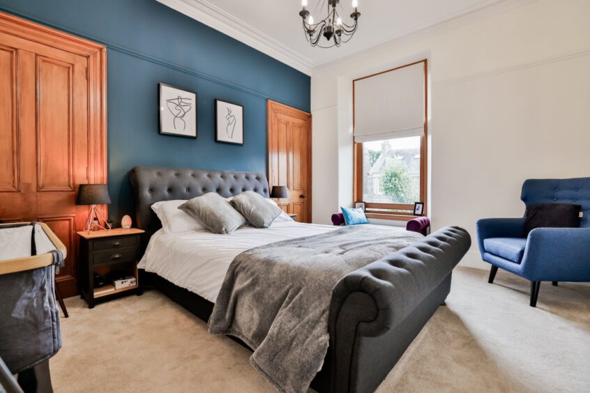 The bedroom in the Aberdeen home after the renovation, with white walls, a dusty dark blue feature wall, a double bed with a grey chesterfield frame and a blue armchair