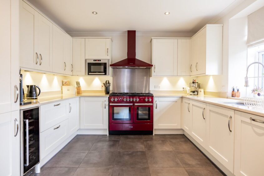 The kitchen is mainly white with lighting under the cabinets, there is a maroon oven and stove hood which gives the room a pop of colour