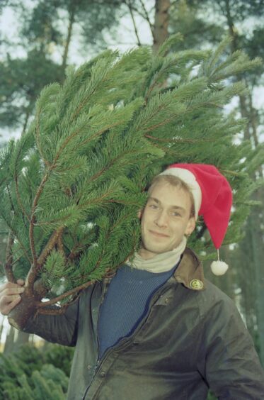 A man carrying a Christmas tree from Kirkhill Forest over his shoulder with a santa hat on