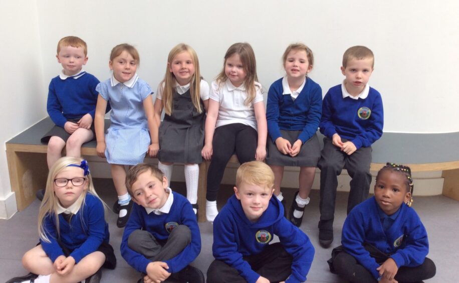 First class of 2023 at Brimmond Primary School. they are sitting in two rows, four pupils sitting on the floor and six pupils sitting on a bench behind them