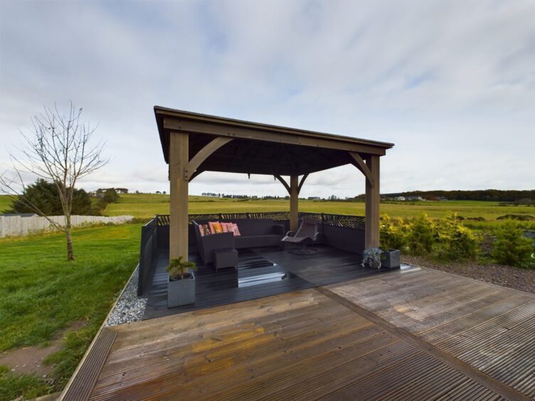 The covered outdoor space with a wooden patio and black patio furniture