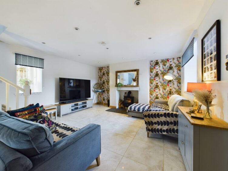 The living area with marble tiles, white walls, two colourful wallpaper panels on either side of the fireplace and two sofas