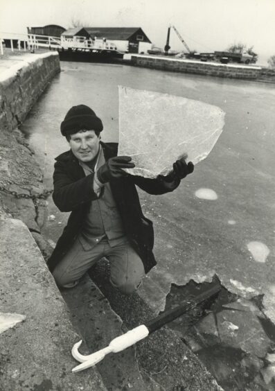 A young man holds up a thick sheet of ice taken from one of the frozen sea locks on the Caledonian Canal in 1987.