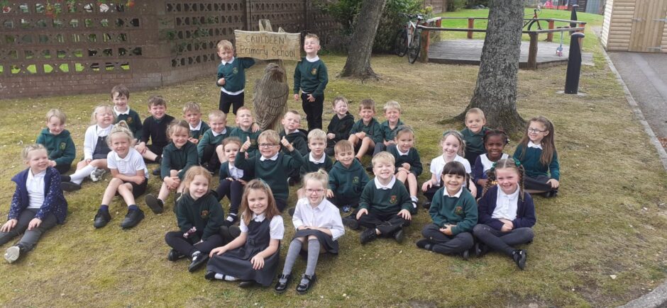 Cauldeen Primary School pupils sitting in rows on the grass outside the school