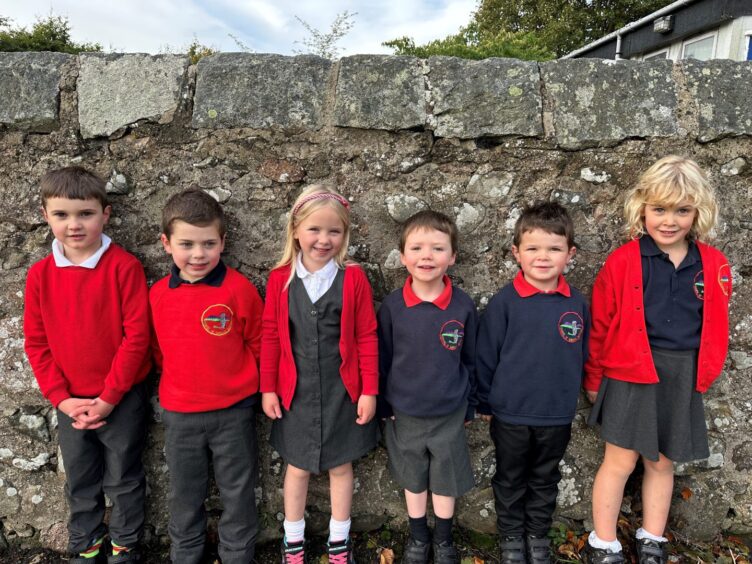 Chapel of Garioch School P1 pupils lined up against a stone wall, smiling for the camera
