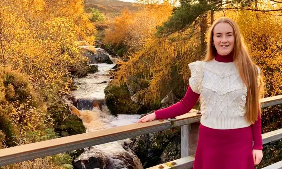 Ciara, pictured on a wooden bridge with a scenic river and forest behind her, is appealing for distillery funding