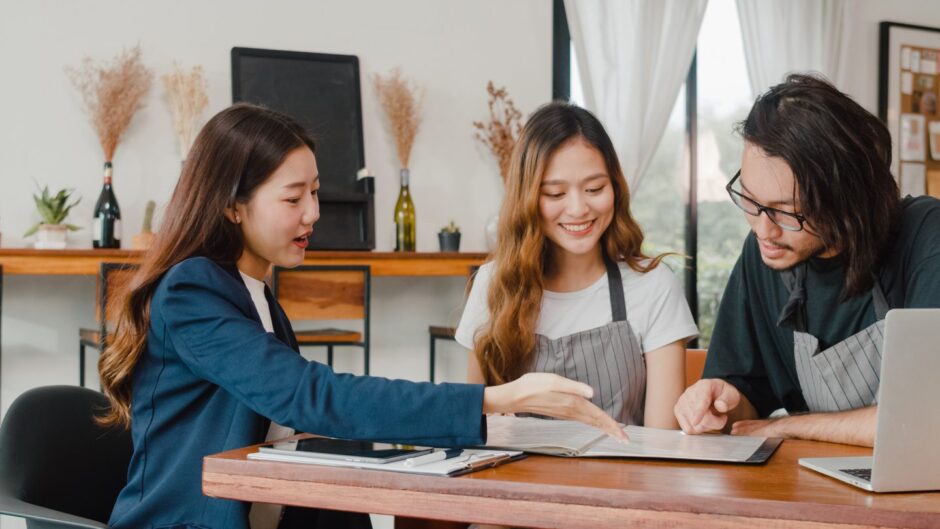 Cheerful Asian small business owners couple meeting with consultant talking about how to sell a business in the UK