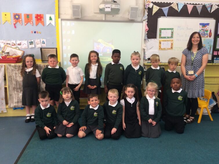 First class of 2023 at Cornhill Primary School in two rows in a classroom with the school crest on a projected screen behind them