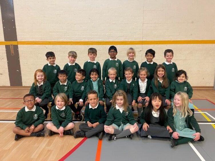 Class P1L at Cults Primary School in Aberdeen, sitting in three rows in the PE hall, they are smiling at the camera for their first class 2023 photo 