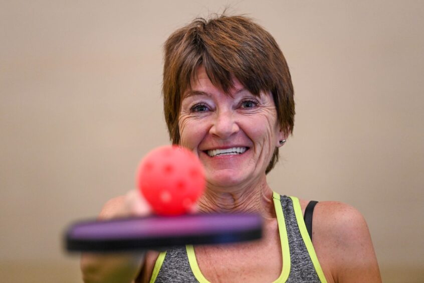 Anna balancing a pickleball on her racket and grinning at the camera