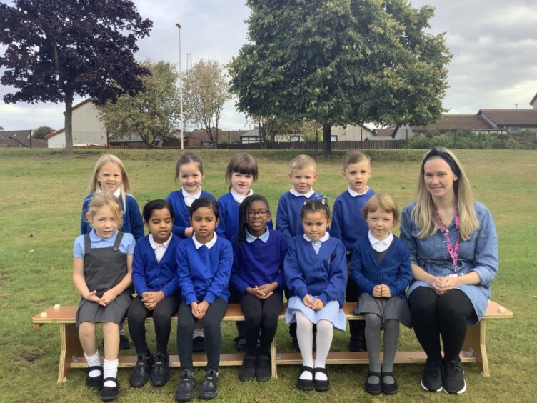 First class of 2023 at Danestone Primary School in Aberdeen with Ms Smith. The children are in two rows, the front row are sitting on bench with their teacher sitting next to them