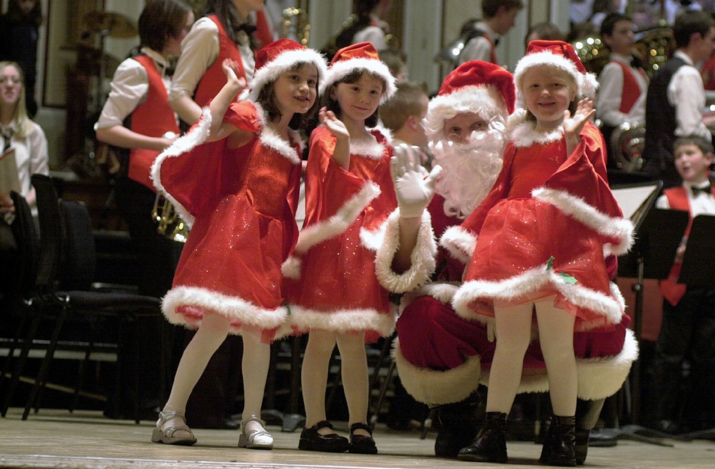 someone dressed as santa kneeling next to three girls in festive costumes