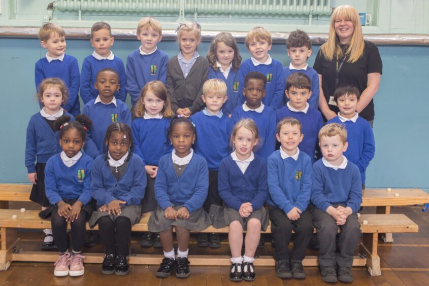 Pupils from class P1MP at Ferryhill Primary School arranged in three rows on benches with their teacher Mrs Murray