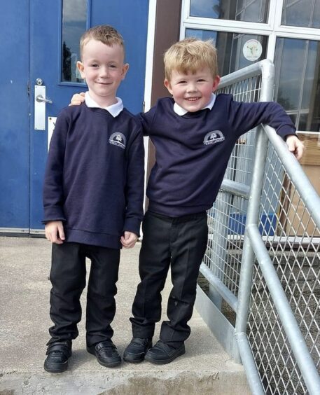 The two primary one pupils at Fintry School standing at the top of the stairs outside the school