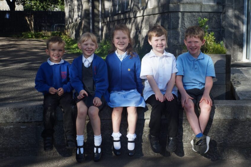 Class P1G at Gilcomstoun School. The five pupils are sitting on a short stone wall outside the school