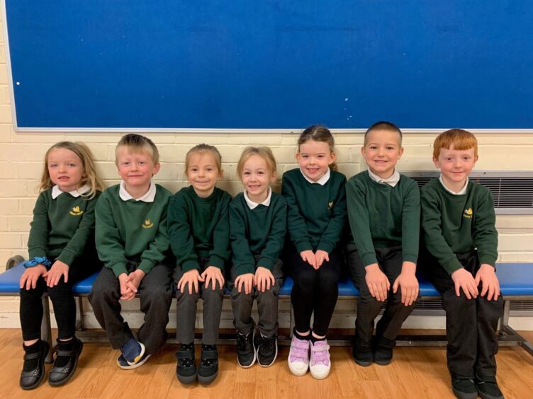 P1-2 of the First class 2023 at Gordon Primary school in Aberdeenshire, sitting on a bench against a wall in a classroom