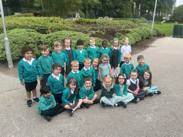 Mrs Stevens Class P1ST at Hazlehead Primary School. The children are in three rows outside, with bushes behind them