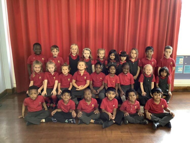 First class of 2023 at Holy Family RC Aberdeen. The children are three rows with a red curtain behind them