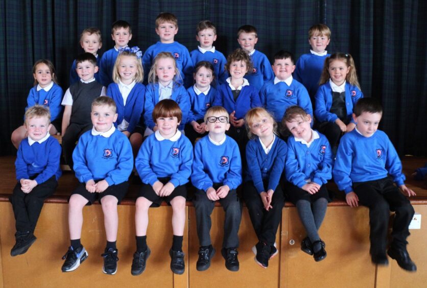 Hythehill Primary School's class P1A on the stage in the assembly hall with a plaid curtain behind them