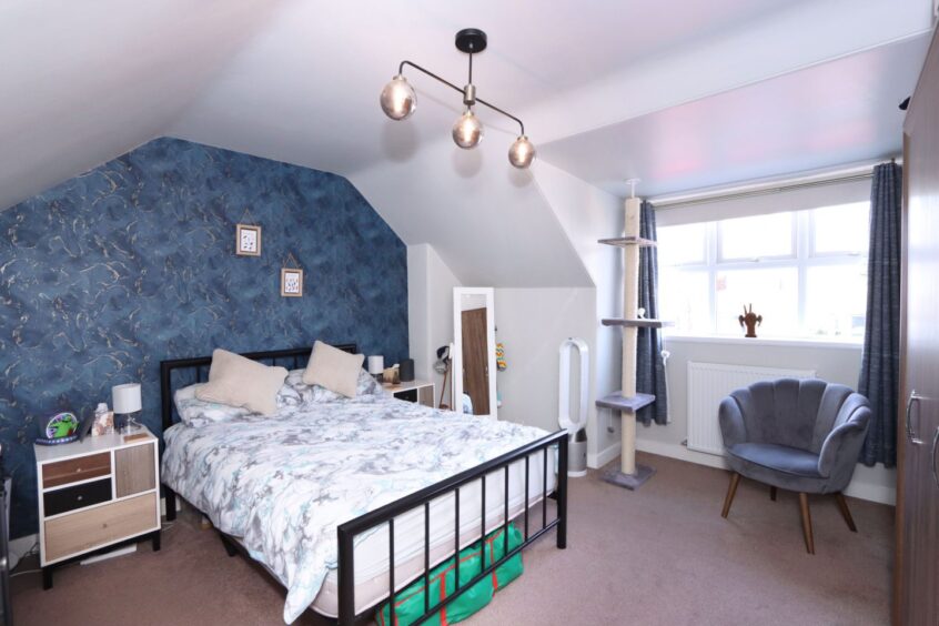 A bedroom in the aberdeen home after the renovation with a blue and gold feature wall, a black metal-framed double bed with two wooden side table, a grey and cream cat tree and a dark blue armchair