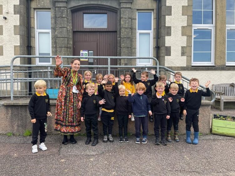 Inverlochy Primary School's P1 class standing outside the school with a teacher, waving at the camera