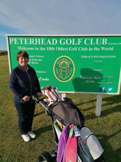 Peterhead Golf Club ladies' champion Irene Young with the club sign behind her and her golf caddy