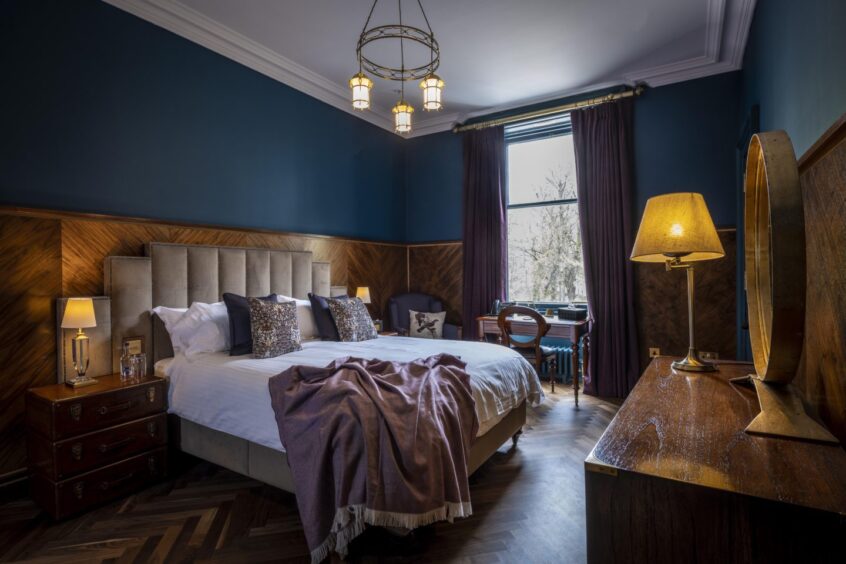 Another bedroom at Linn House, featuring herringbone flooring, deep blue walls and luxurious bedding.