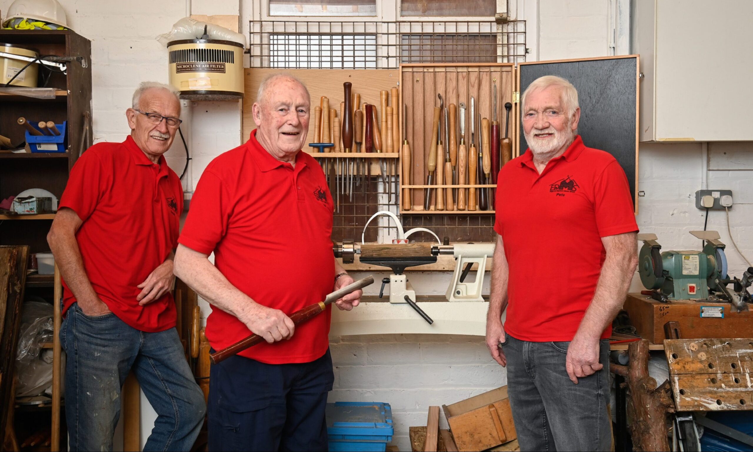 Three men in workshop with tools behind. 
