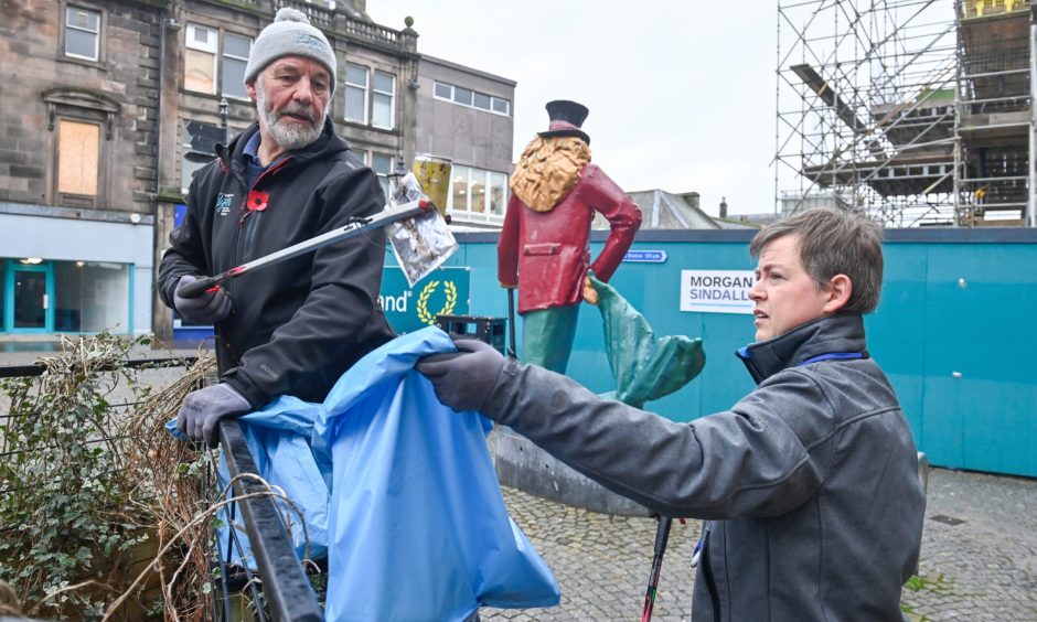 Rubbish lifted on Elgin High Street and dropped into blue bin bag.