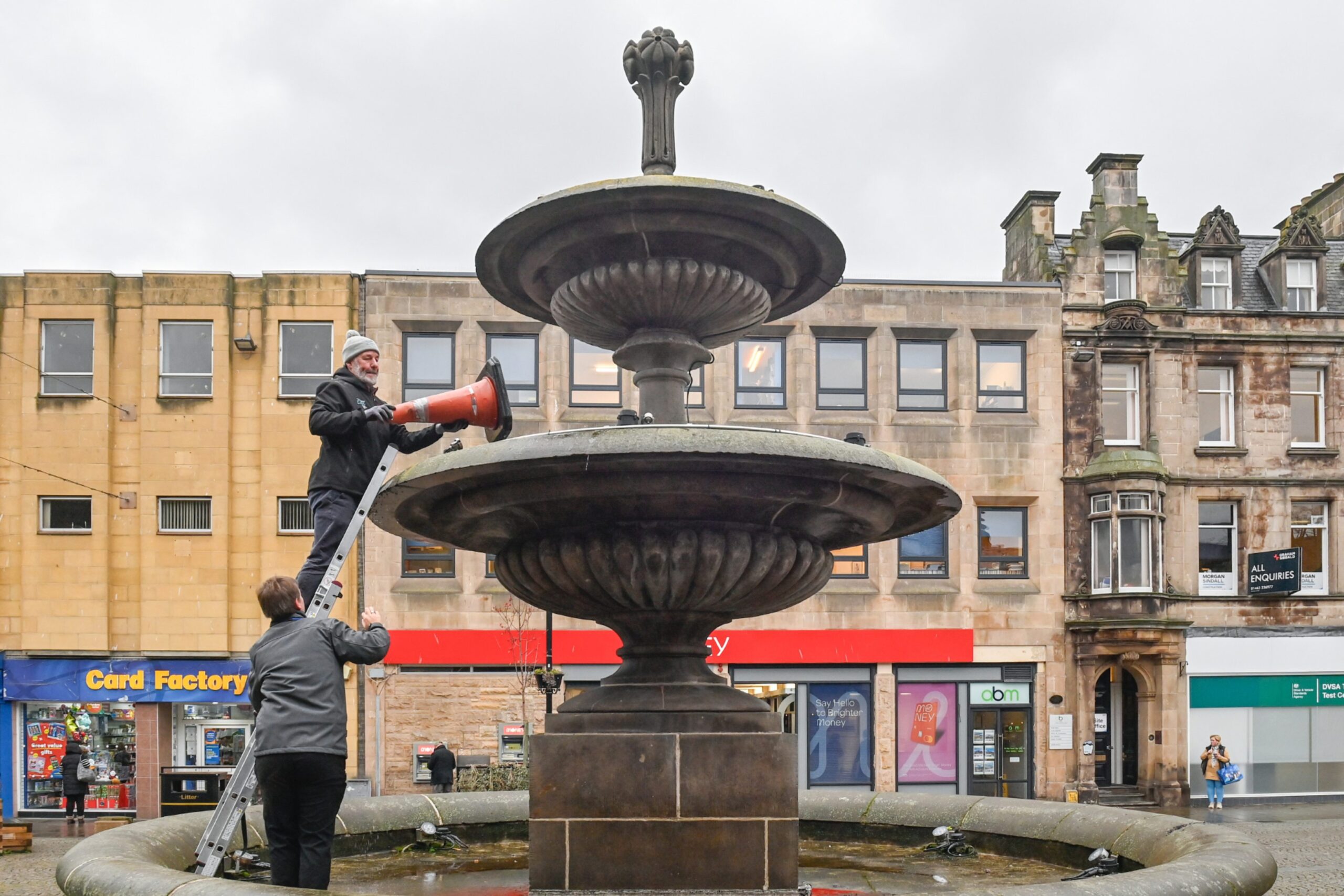 Traffic cone being lifted out of Elgin High Street fountain using stepladder.