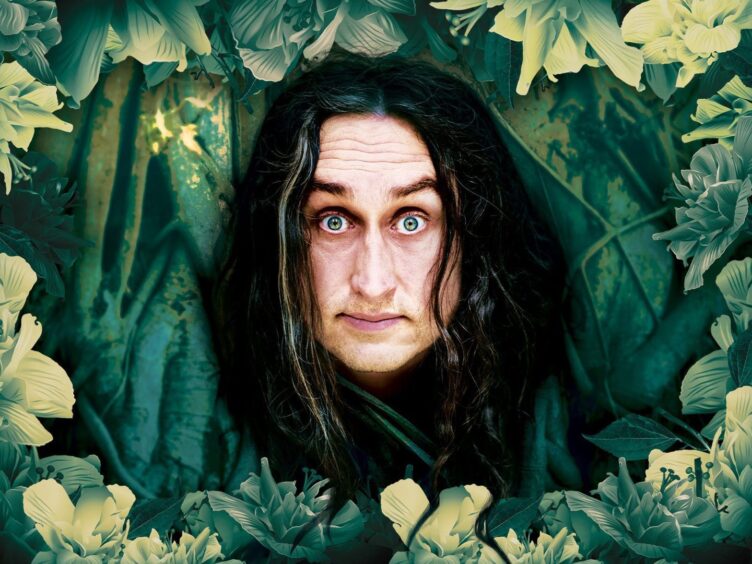 Ross Noble with his head popping through a green stage dressing