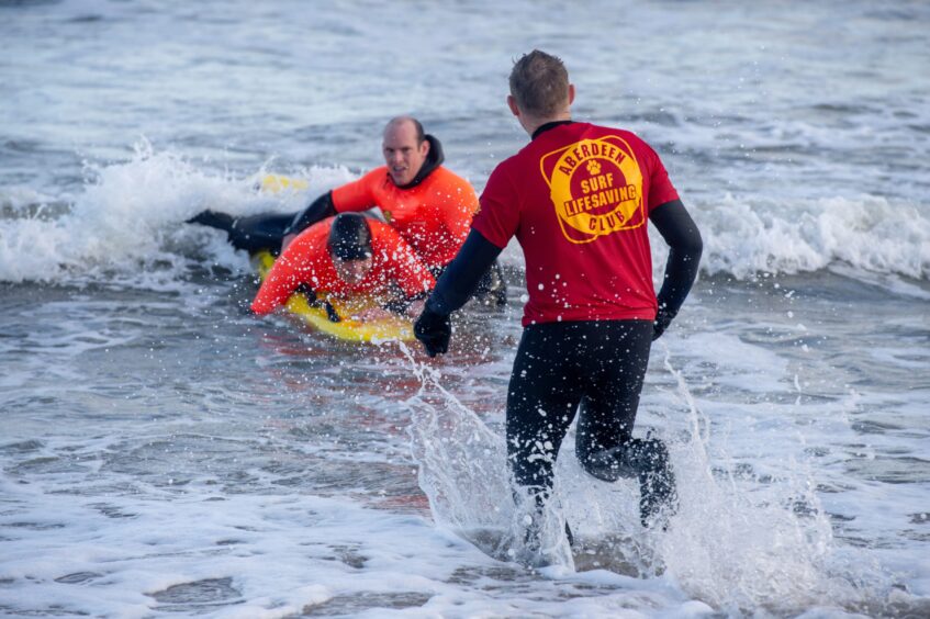 Adam Rofe and Chris Leach demonstrate a rescue exercise on surf board in the sea.