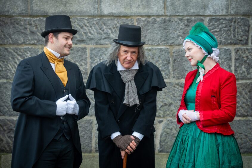 Three cast members in costume, with a granite wall behind them