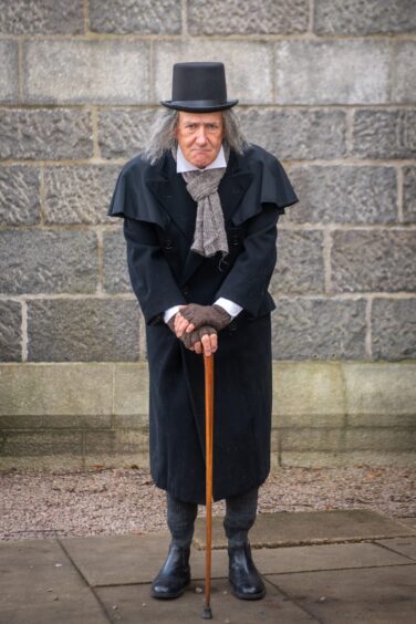 Colin Campbell dressed at Scrooge with both hands on the walking stick looking at the camera outside Ferryhill Parish Church, Aberdeen. 