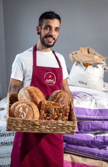 Claudio in a SourCloud apron, holding a basket of different breads