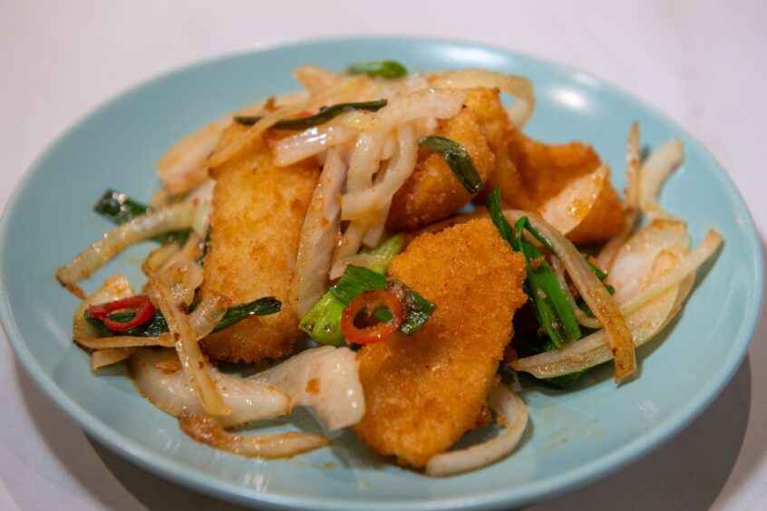 Breaded calamari with onions, chilli and spring onions on a blue plate. 