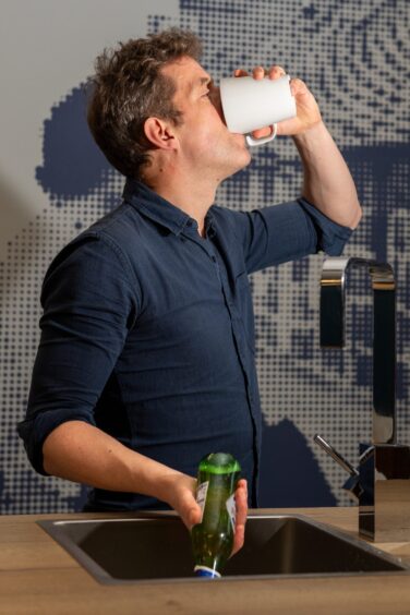 Andy Morton drinks from a cup of coffee as he pours beer down a sink.