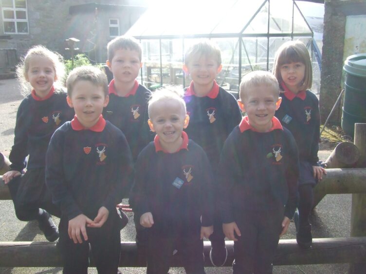 Seven Keithhall Primary School pupils from the first class of 2023 sitting outside the Aberdeenshire school, a greenhouse behind them.