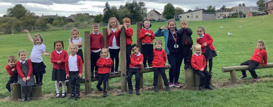 Class P1NK at Kingsford School standing and sitting along an obstacle course in a park with their teacher