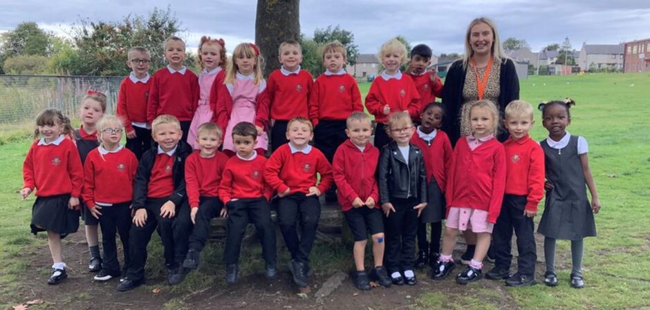 Class P1RW at Kingsford School standing in two rows in front of a tree on the school grounds with their teacher