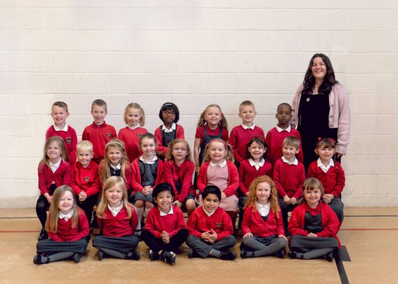 Class P1AS at Kingswells School arranged into three rows in the PE hall with their teacher standing next to them