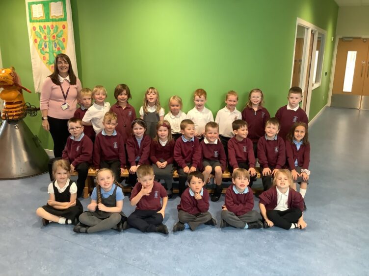 Class P1K at Kintore Primary School in the bright green lobby of the school with their teacher