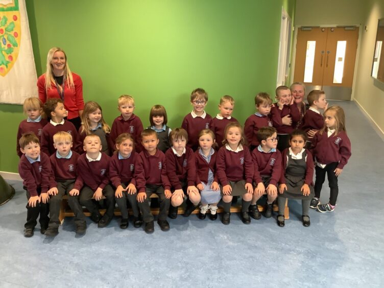 Class P1S at Kintore Primary School in two rows standing in the brightly coloured lobby of the building