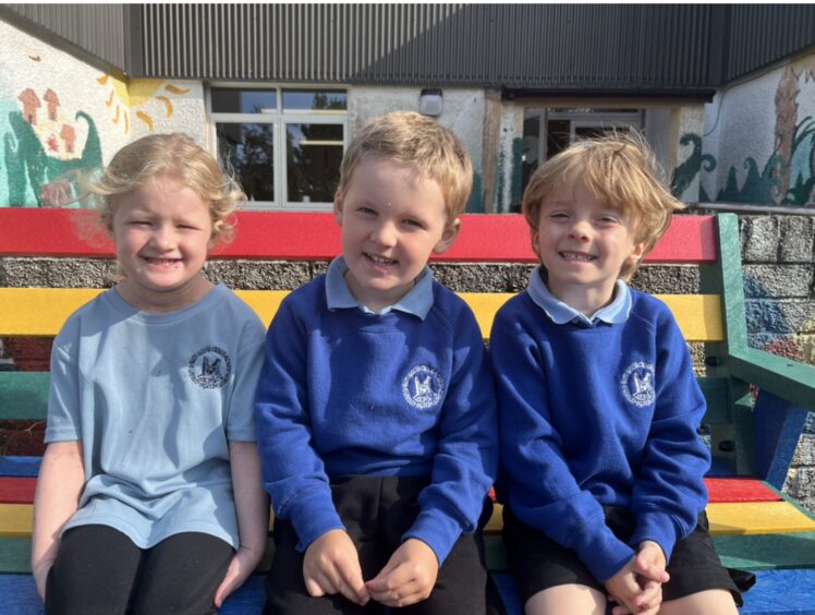 Three Kyleakin Primary School's pupils sitting on a rainbow-coloured bench in the playground
