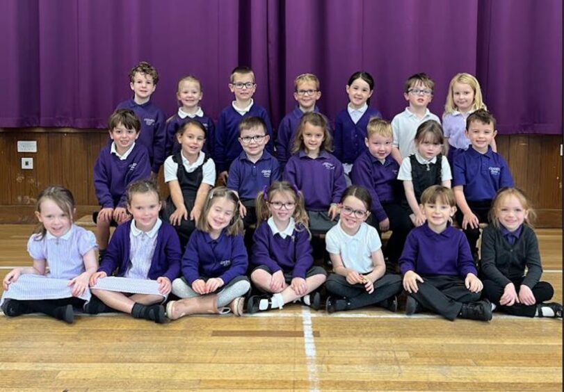 Class P1B at Lochardil Primary School, Inverness in the assembly hall with a purple curtain behind them