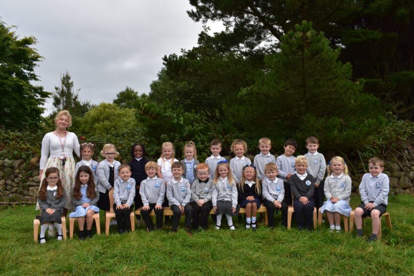 A Loirston Primary School Primary one class sitting in two rows on the grass outside the school with their teacher